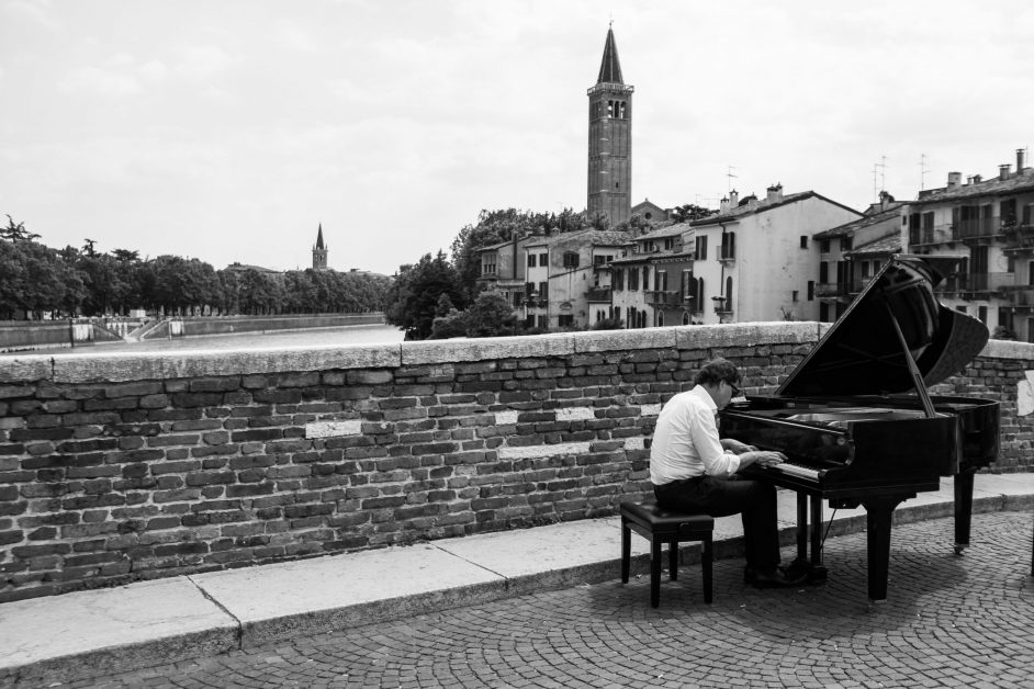 man playing grand piano on stone bridge over river